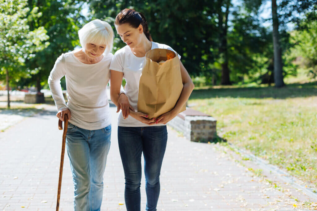 For fall prevention, a woman is walking with a cane and assistance
