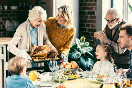 An older woman carries a turkey to the table as her family looks on and prepares for a healthy Thanksgiving.