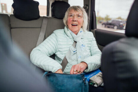 A senior woman sitting in the back of an Uber or Lyft while smiling and looking up.