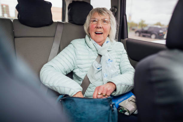 A senior woman sitting in the back of an Uber or Lyft while smiling and looking up.