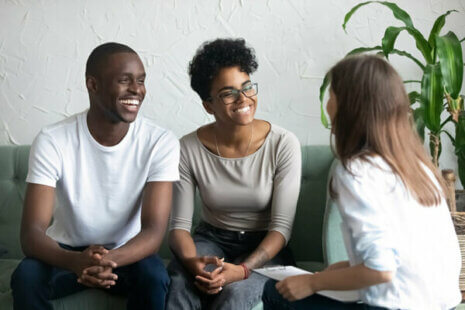 Two adults are sitting side by side and smiling, facing an elder mediator.