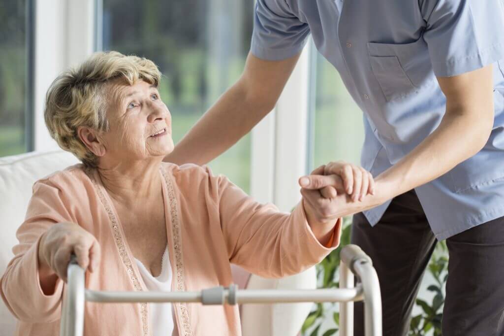 Old woman gets help with walking from a nurse