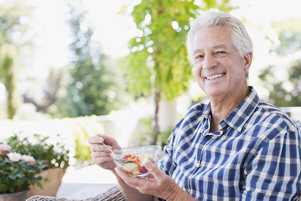 Senior man eating vegetables on patio