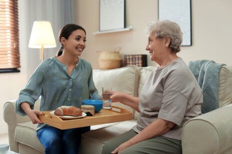 In-home senior care caregiver serving dinner for a client.