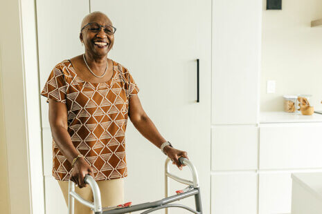 A woman stands smiling and holding onto a walker as she focuses on fall prevention for seniors.