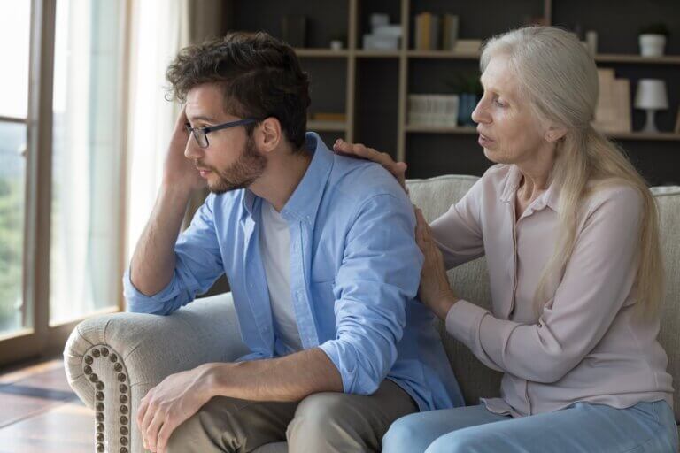 caregiver burnout during the holidays — adult son looking stressed while helping his aging mother at home during the holiday season