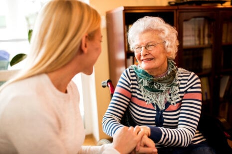 Adult child sitting with aging parent at kitchen table, having a compassionate conversation about talking to parents about accepting home care